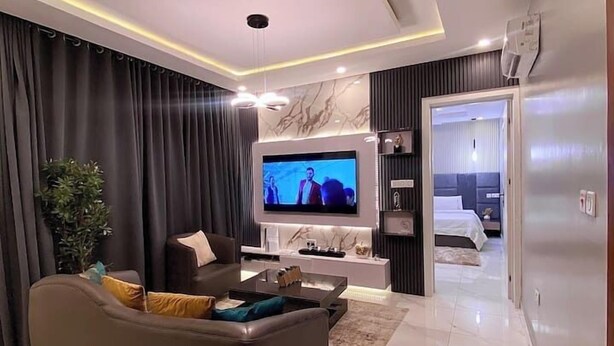 Een moderne woonkamer met een grote flatscreentelevisie, een donkere bank en een salontafel.