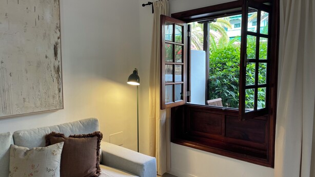 Een kamer met een witte bank, een lamp en een raam met uitzicht op groen.