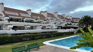 Een hotel met meerdere verdiepingen, balkons, een zwembad en groene bankjes.