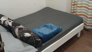 A single bed with a grey mattress, a blue pillow, and a patterned pillow on a white frame. - Cozy City Stay in Baguio (Baguio City)