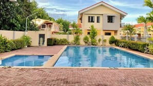 A swimming pool area with two pools, surrounded by a brick walkway and greenery.