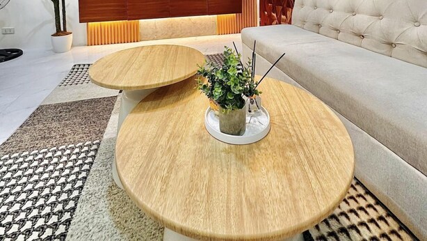 A modern living room with a flat-screen TV, wooden shelves, a sofa, and two round wooden tables.