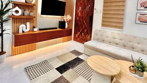 A modern living room with a flat-screen TV, a wooden entertainment unit, a beige sofa, and a patterned rug.