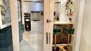 A modern kitchen with white cabinets, a gas stove, and a microwave. There are two green bar stools and a decorative plant on the counter.