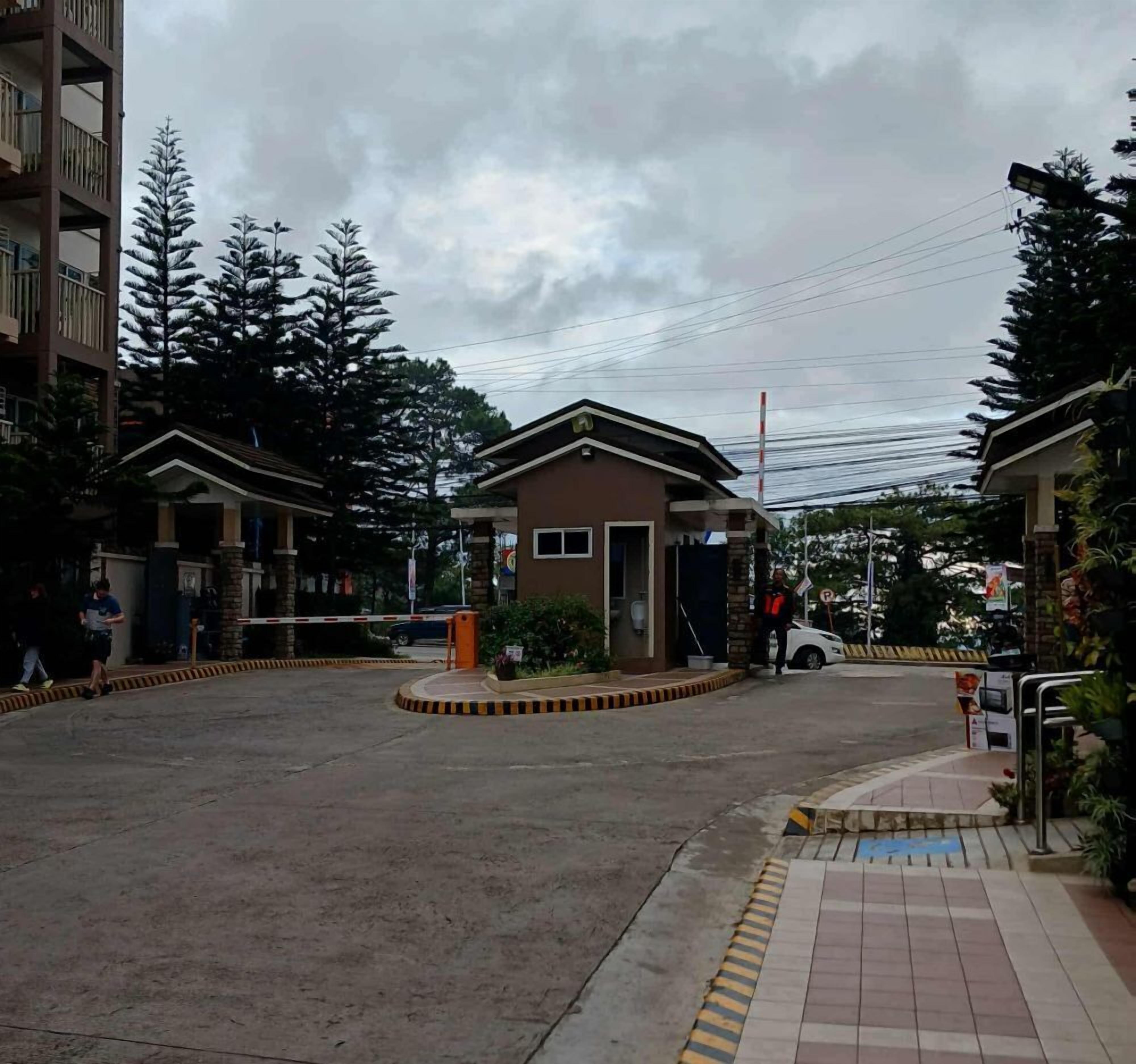 A gated entrance to a residential area with a small building, a gated driveway, and a pedestrian pathway.