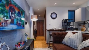 Een moderne woonkamer met een bruine bank, een aan de muur bevestigde televisie, en een eethoek met een tafel en stoelen.