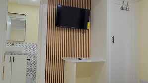 Una camera d'albergo con un letto, una televisione fissata al muro e un bagno visibile attraverso una porta aperta.