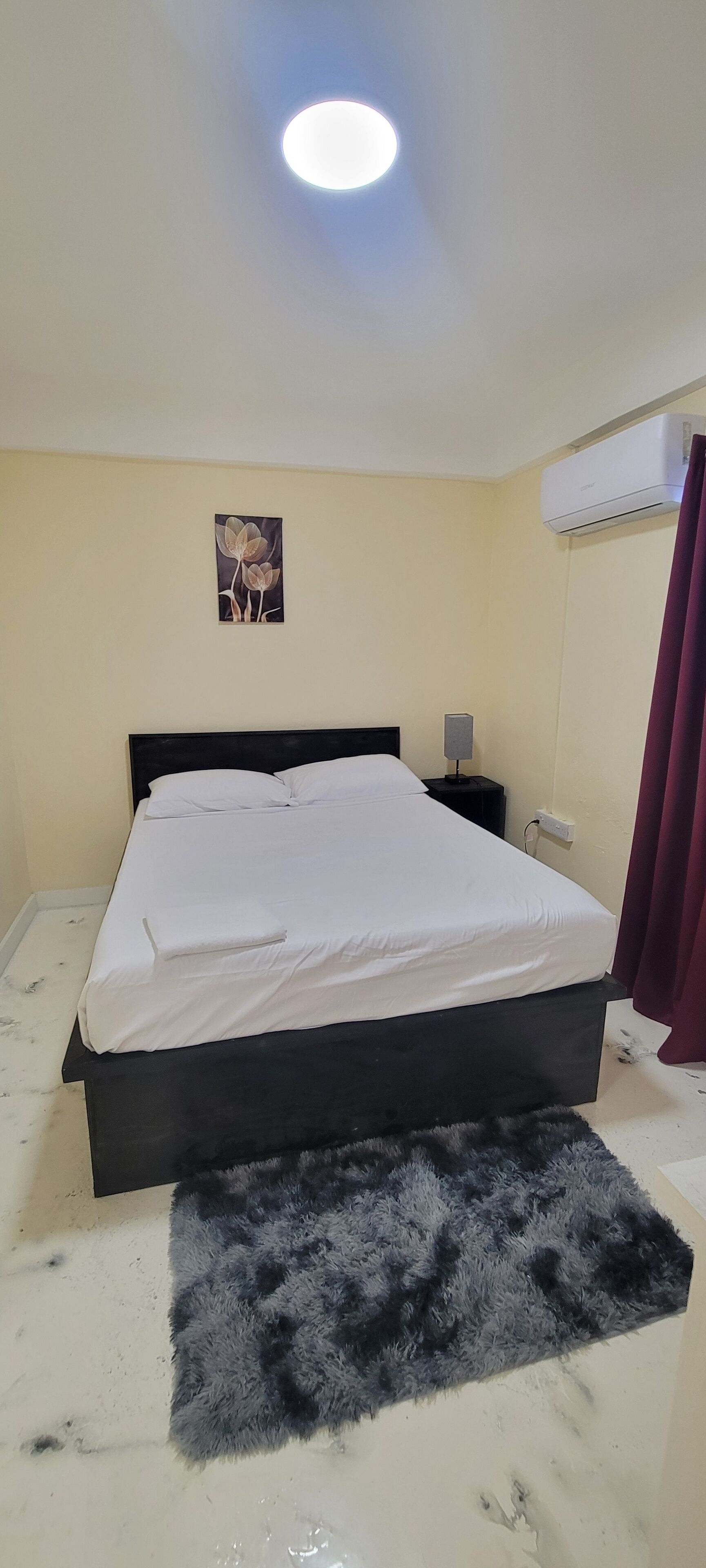 A bedroom with a bed, a nightstand, a wall-mounted air conditioner, and a painting.