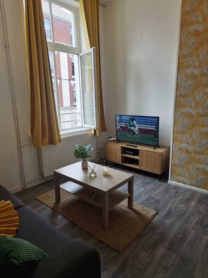 A living room with a television, a coffee table, a sofa, and a window with curtains.