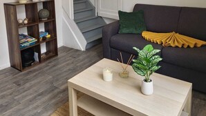 Een woonkamer met een bank, een salontafel, een boekenkast, een trap en een deur.