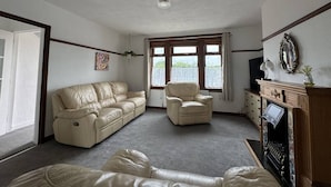 En stue med en beige sofa, en lænestol og en pejs.
