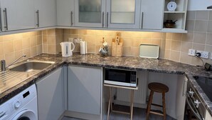 Una cocina compacta con armarios blancos, encimera de granito, microondas integrado, cafetera y un taburete de madera.