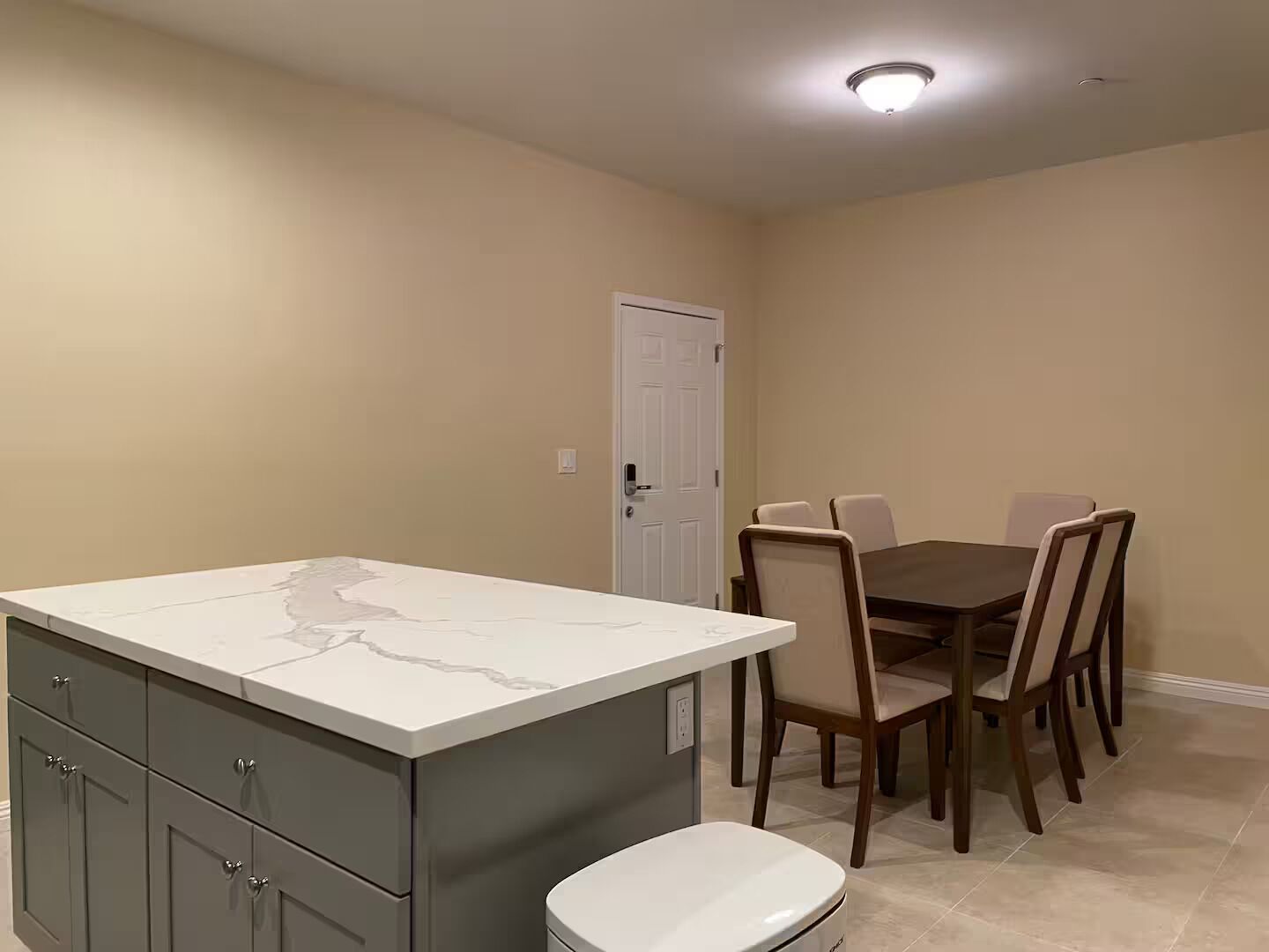 A kitchen with a marble countertop, wooden cabinets, a dining table with chairs, and a white door.