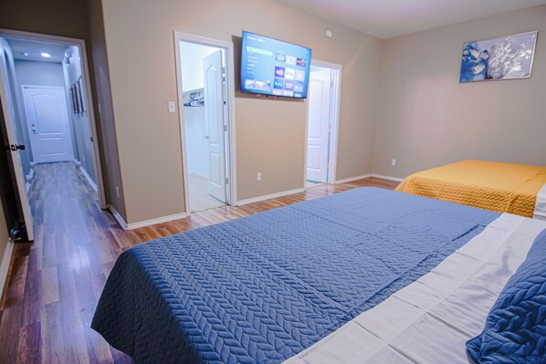 A bedroom with a large bed, a television mounted on the wall, and a hallway leading to another room.