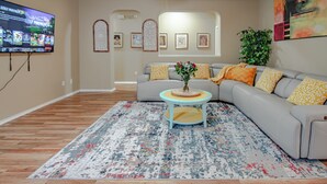 A living room with a grey sofa, a coffee table with a vase, a patterned rug, and a TV on the wall.