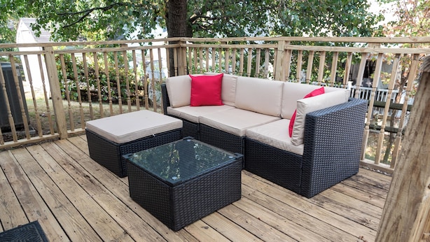 Eine Holzterrasse mit einem Korbusofa und einem Couchtisch mit Glasplatte.
