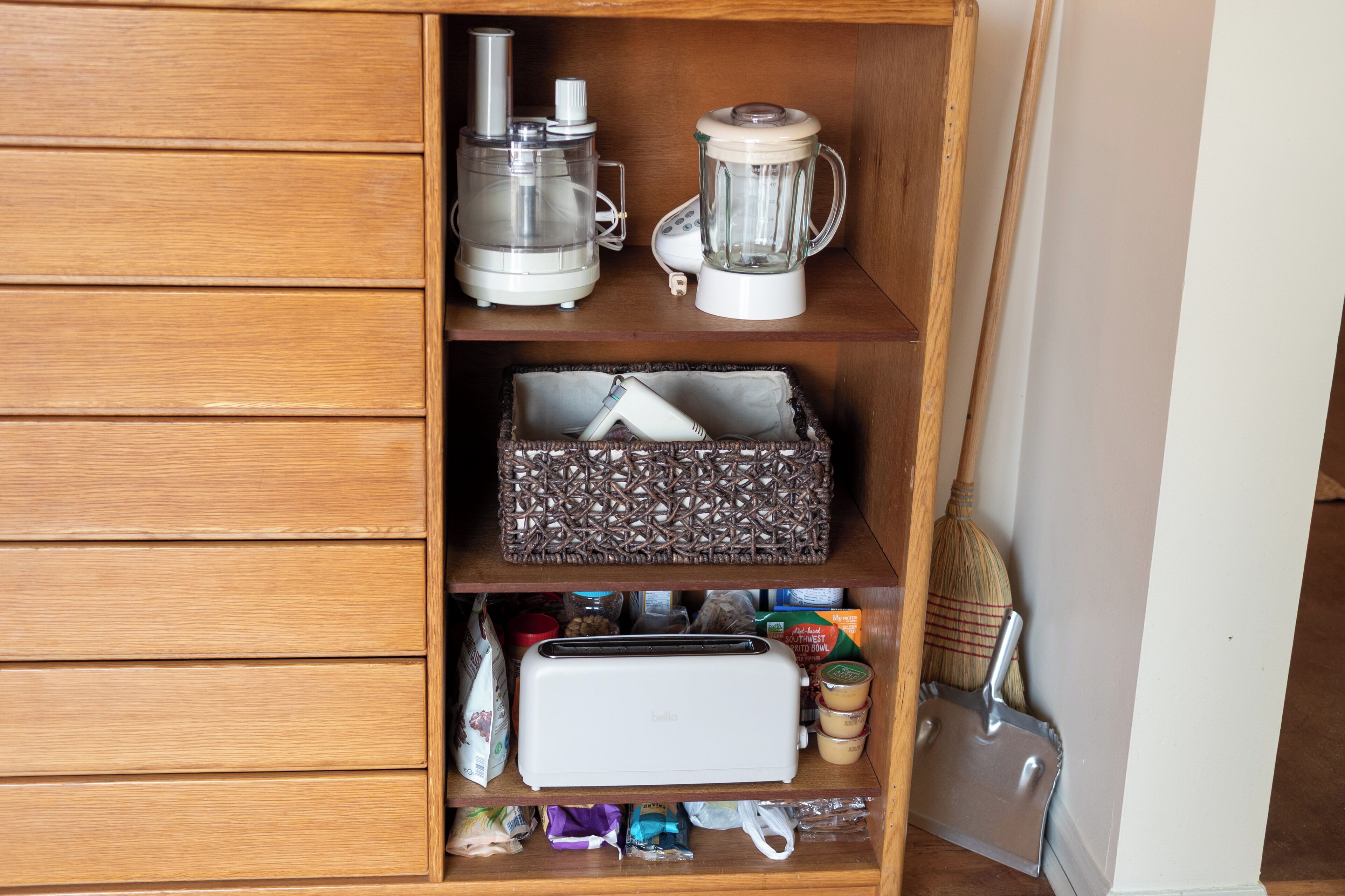 A kitchen with a food processor, blender, toaster, and various kitchen items on shelves.