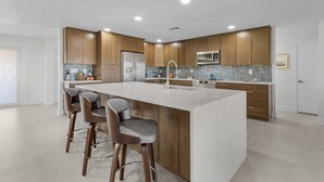 A modern kitchen with wooden cabinets, a central island with bar stools, stainless steel appliances, and a tiled backsplash.