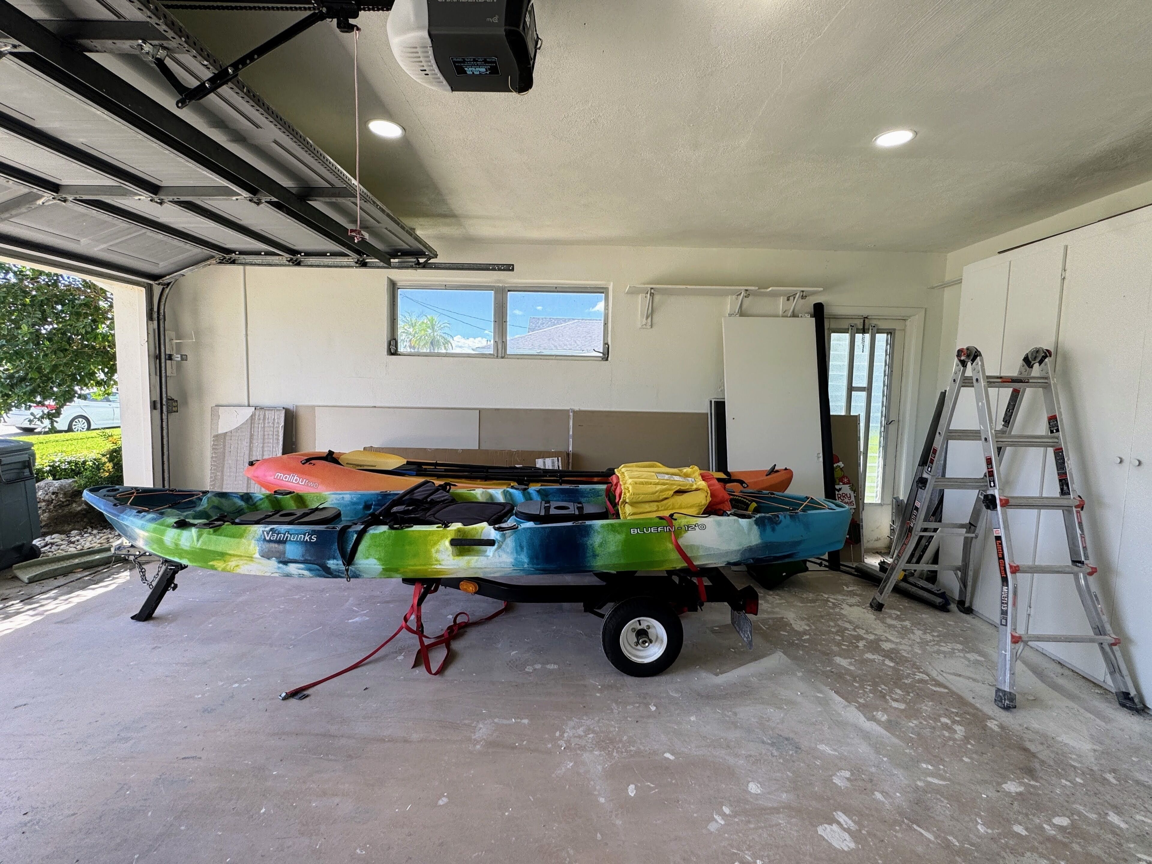 Un garage con un kayak su un rimorchio, una scala e una porta che dà sull'esterno.