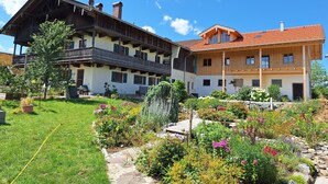 Un chalet traditionnel avec une façade en bois, un toit en pente et un jardin bien entretenu, agrémenté de fleurs colorées et d’un chemin en pierre.