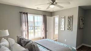 Ein Schlafzimmer mit einem Bett, einem Deckenventilator, einem Fenster mit Vorhängen und einer Tür.