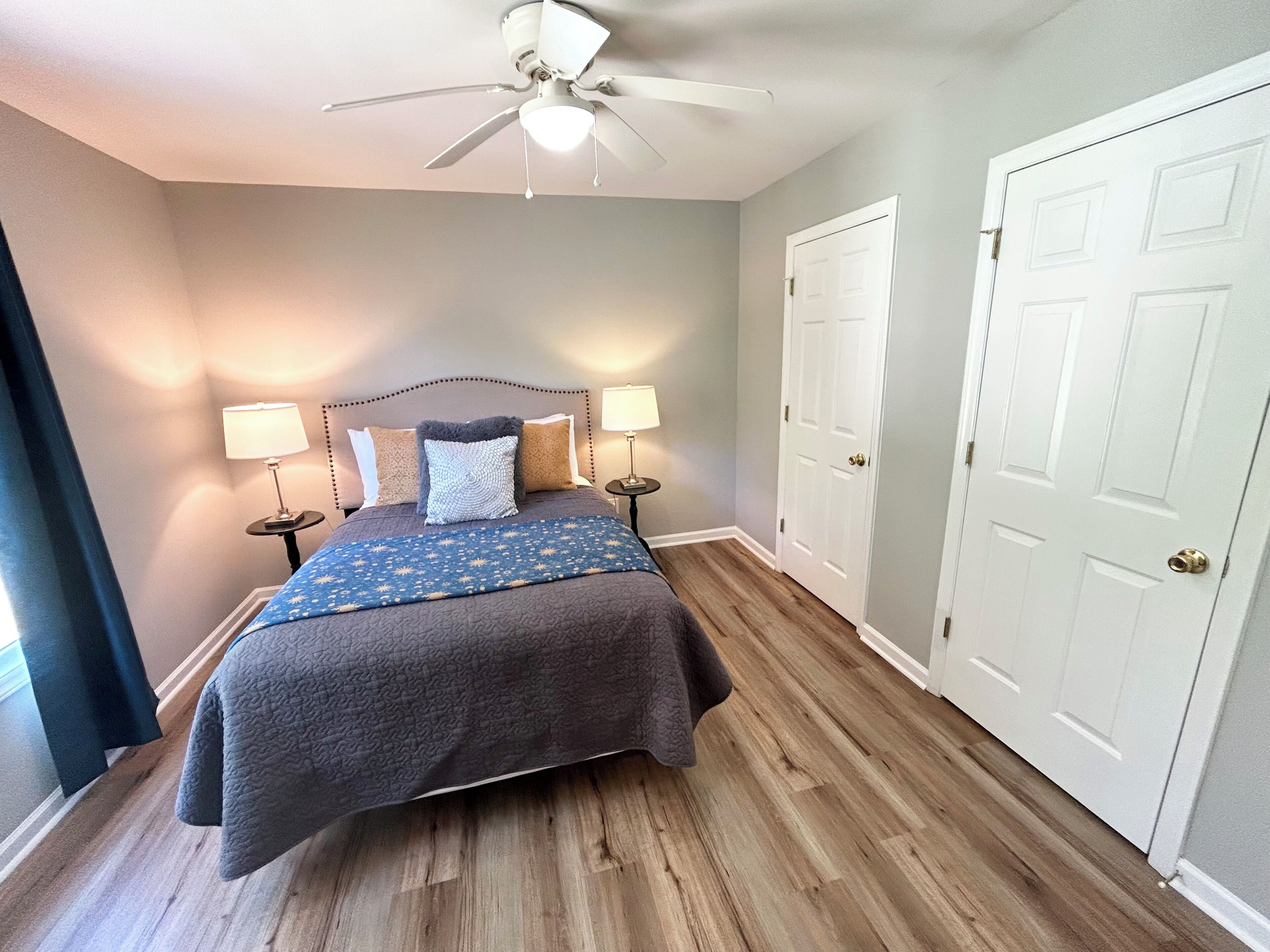 Une chambre à coucher avec un lit, deux lampes de chevet, un ventilateur de plafond et une porte.
