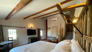 A bedroom with a large bed, wooden beams, a TV, a desk, and a chair. - Farmhouse With Swimming Pool in Provence (Violes)