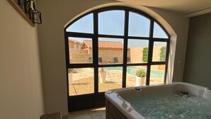 A bathroom with a large arched window, a bathtub, and a view of a swimming pool and buildings outside. - Farmhouse With Swimming Pool in Provence (Violes)
