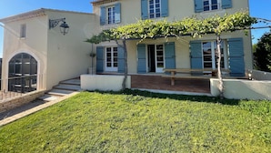 A two-story house with a covered patio, a stone staircase, and a well-maintained lawn. - Farmhouse With Swimming Pool in Provence (Violes)