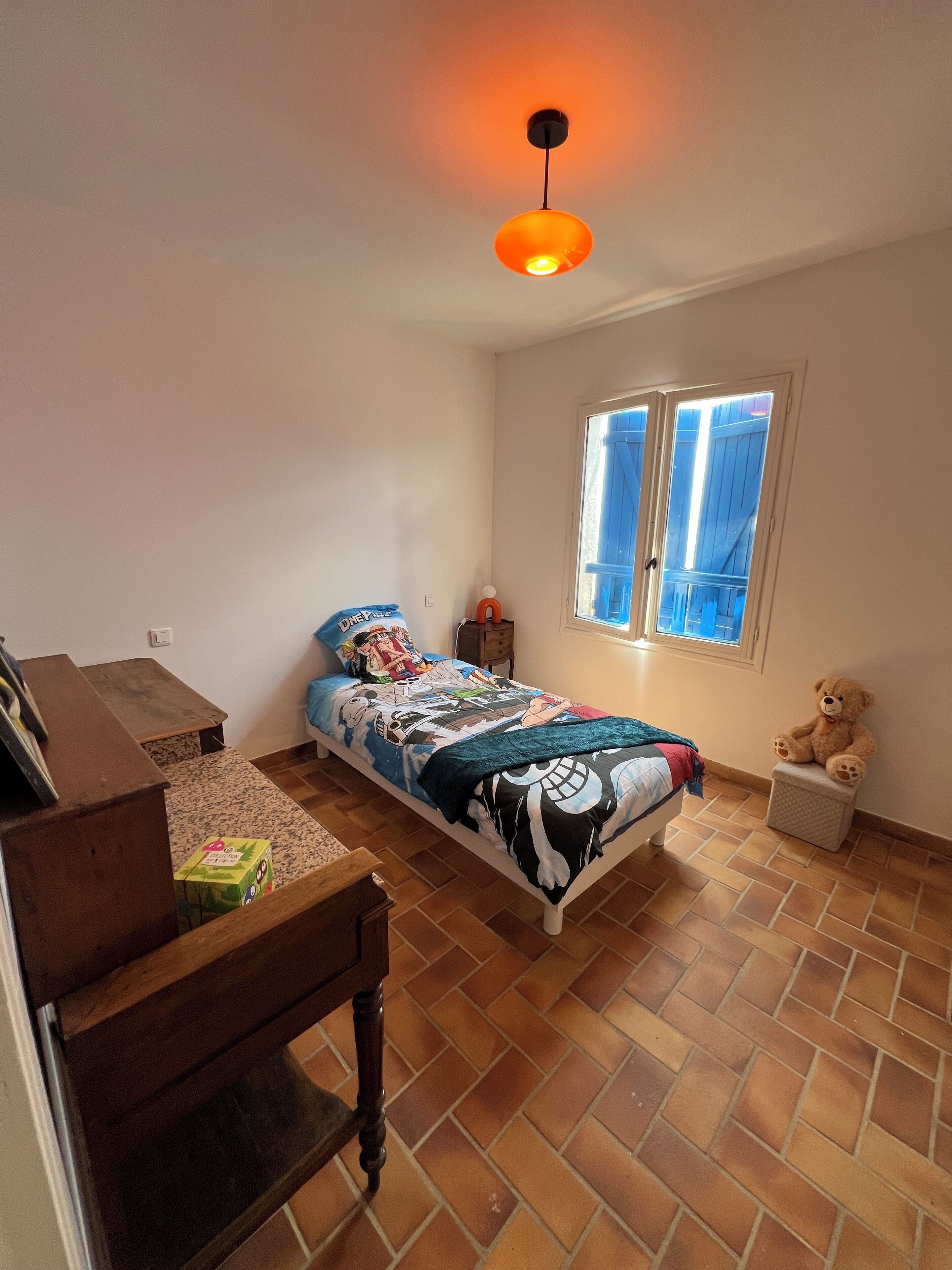 A bedroom with a bed, a desk, a chair, a window, and a teddy bear.