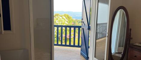 An open door leading to a balcony with a blue railing, a wooden dresser, and a mirror.