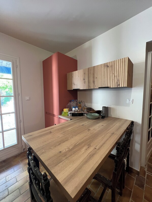 A kitchen with a wooden table, a red cabinet, and a wooden hanging shelf.