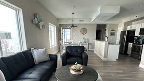 A spacious living room with a black leather sofa, a round coffee table, and a dining area with a white table and chairs.