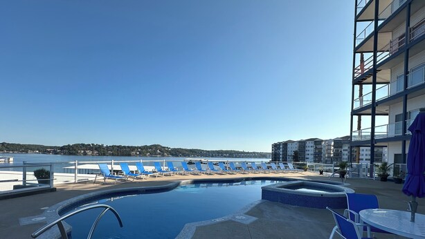 A pool area with a view of the beach, lounge chairs, and a dining table.