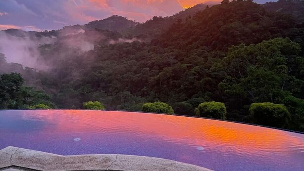 Ein Infinity-Pool mit Blick auf einen bewaldeten Hang und einen Sonnenuntergang.