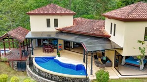 Ein zweistöckiges Haus mit Swimmingpool, Sitzgelegenheiten im Freien und einer überdachten Terrasse.