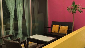 Un balcon avec des meubles en osier, une porte vitrée et un mur rose.