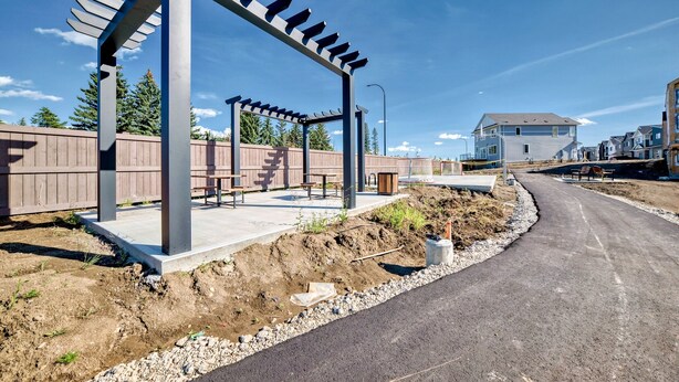Un barrio residencial con un sendero pavimentado, una estructura de pérgola y casas al fondo.