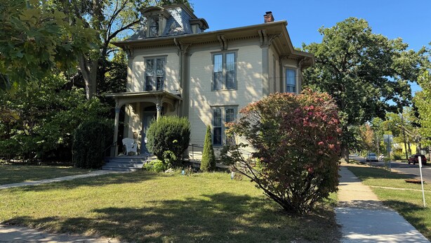 Ein zweistöckiges Haus mit Veranda, Schornstein und gepflegtem Rasen.