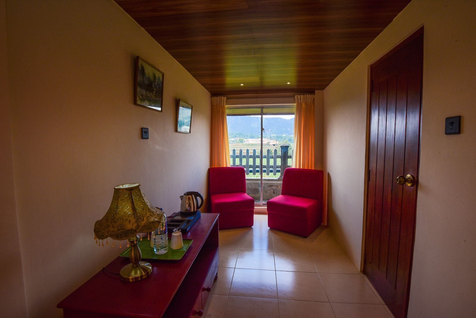 Una habitación con techo de madera, un sofá rojo, una mesa con lámpara y vistas al exterior a una cerca y follaje.