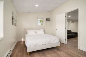 A bedroom with a bed, a door leading to another room, and a window with a view of trees. - 3BR Beach Apartment | The Beachside Co. #12 (Sylvan Beach)