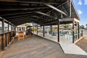 An outdoor covered patio with a barbecue grill, seating area, and a golf cart. - 3BR Beach Apartment | The Beachside Co. #12 (Sylvan Beach)
