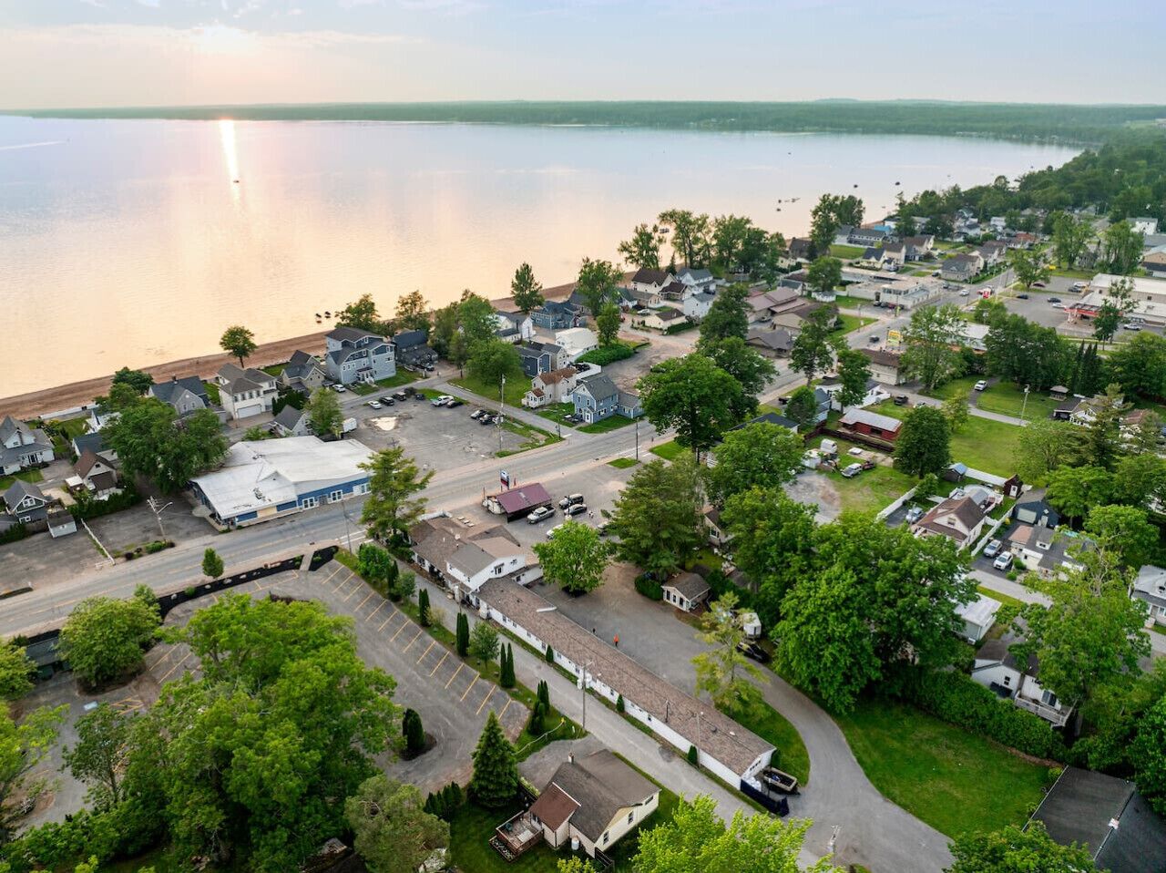 Vue aérienne d’un quartier résidentiel au bord d’un lac, avec des maisons, un parking et un grand bâtiment doté d’un toit bleu.