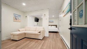 Ein Zimmer mit einem beigefarbenen Schlafsofa, einem Bett mit weißer Bettwäsche, einem Flachbildfernseher an der Wand und Holzboden.