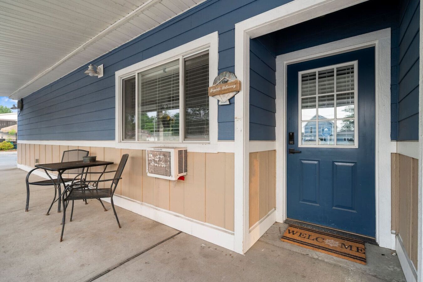 A blue house with a white door, a window with a sign, and a table with chairs outside.