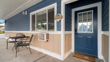 A blue house with a white door, a window with a sign, and a table with chairs outside.