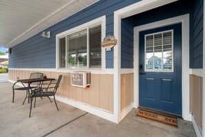 A blue house with a white door, a window with a sign, and a table with chairs outside.
