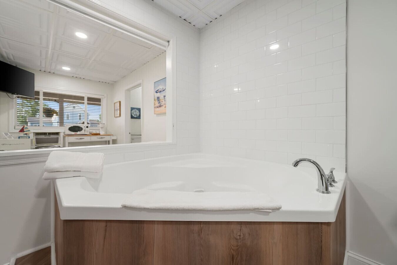 Une salle de bain moderne avec une grande baignoire, un meuble-lavabo en bois, des murs recouverts de carreaux blancs et un miroir au-dessus du lavabo.