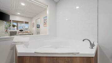 Une salle de bain moderne avec une grande baignoire, un meuble-lavabo en bois, des murs recouverts de carreaux blancs et un miroir au-dessus du lavabo.