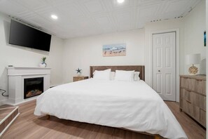 A bedroom with a large bed, a fireplace, a TV mounted on the wall, and a door to the right.